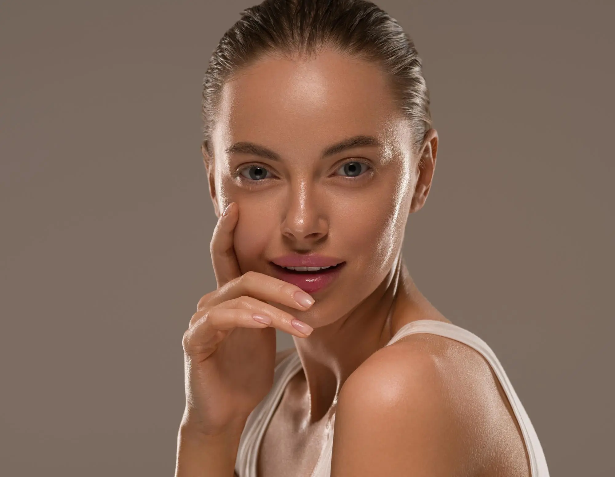 A woman with slicked-back hair showcases glowing skin after skin resurfacing at Refresh MedSpa, on a neutral background.