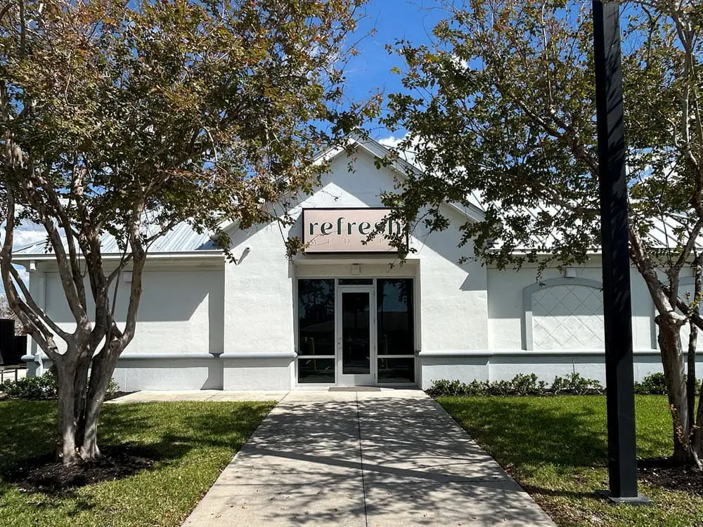 White building with a peaked roof and front door, flanked by trees at Refresh Medspa, the trusted medical spa in Cape Coral, FL.