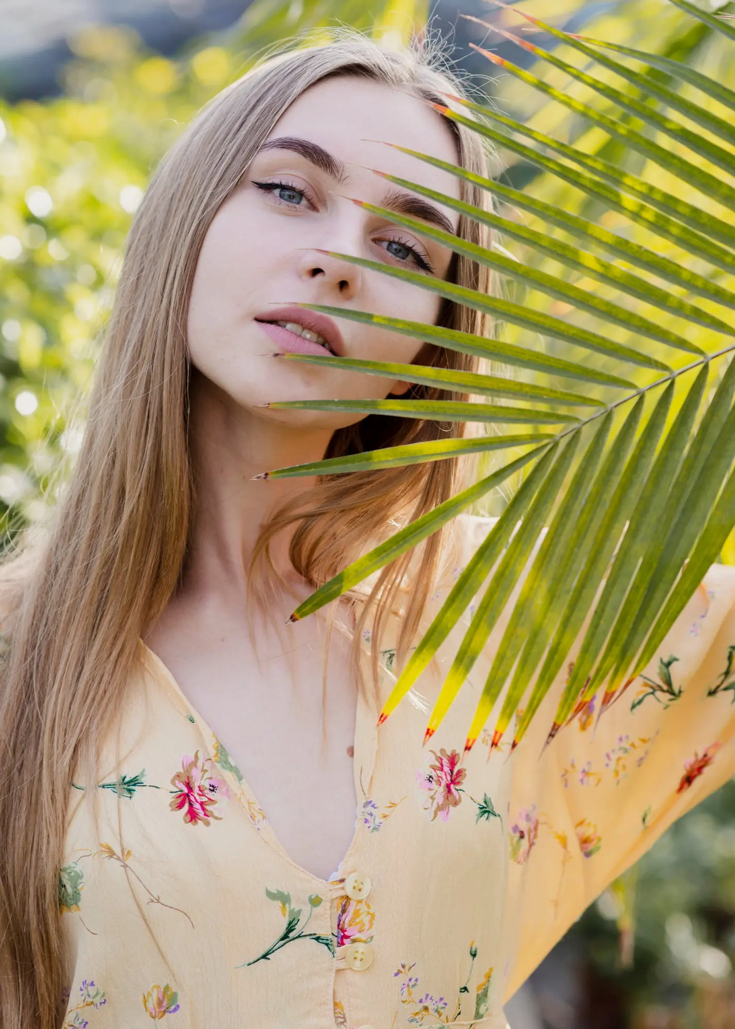 Outdoors in Cape Coral, FL, a woman with flawless skin stands near palm leaves; Refresh MedSpa treats spider veins and vessels.