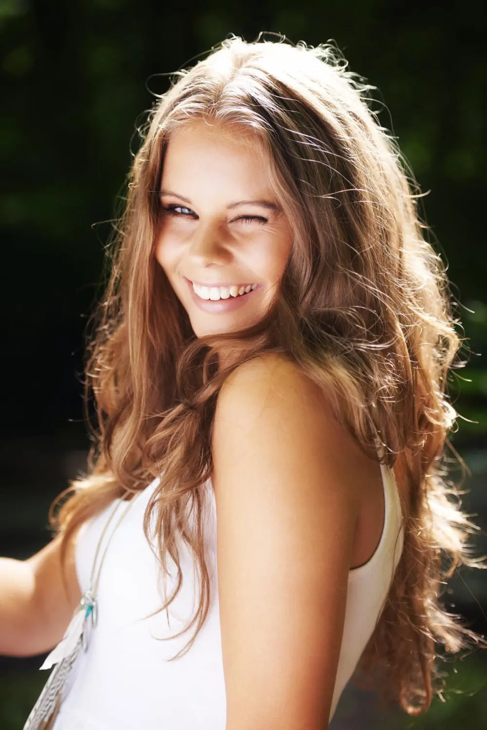 Smiling, winking young woman with clear skin after facial redness treatment at Refresh MedSpa in Cape Coral, FL outdoors in sunlight.