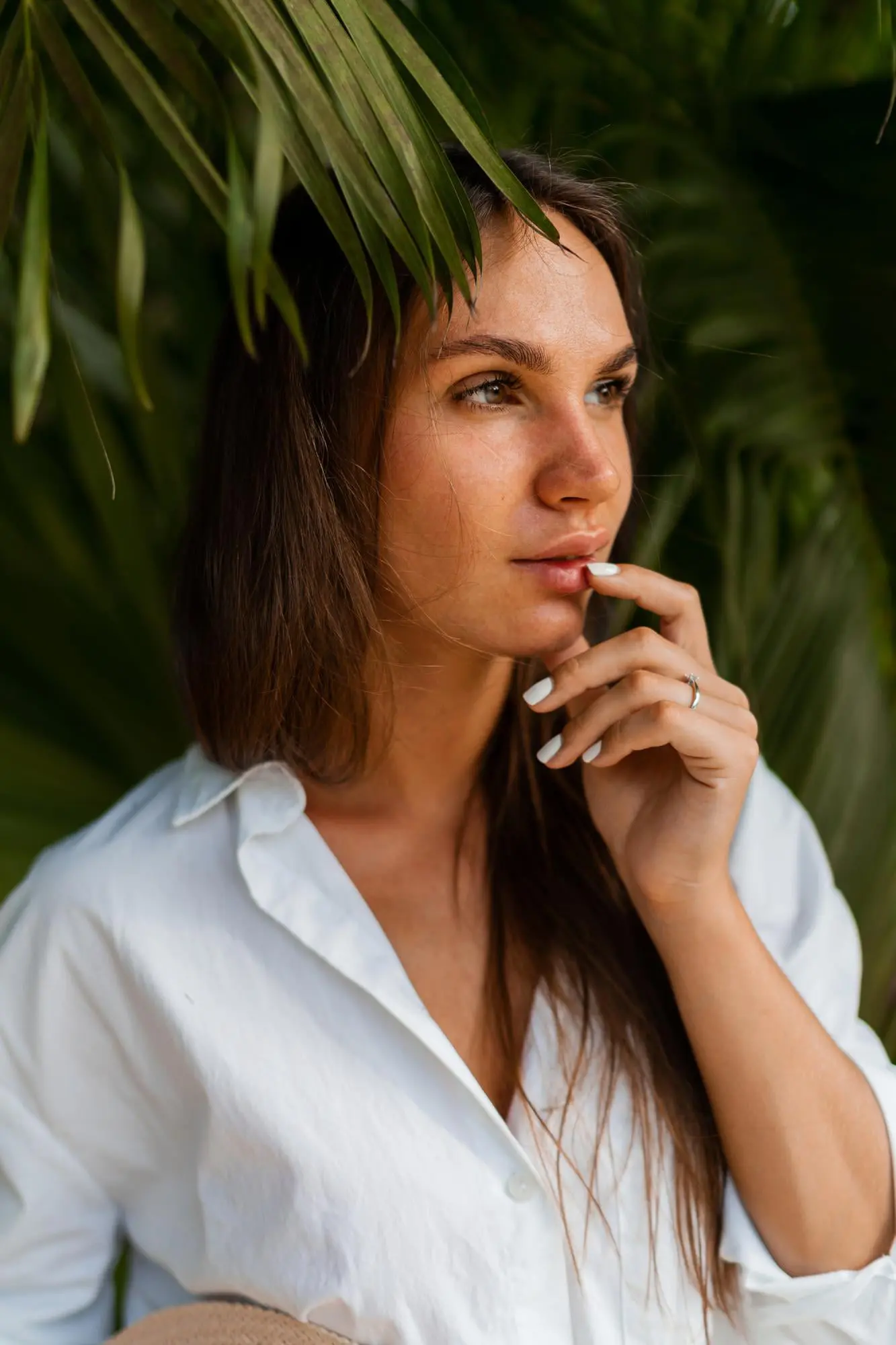 A person in a white shirt stands by green foliage, pondering dull skin at Refresh MedSpa in Cape Coral, FL.