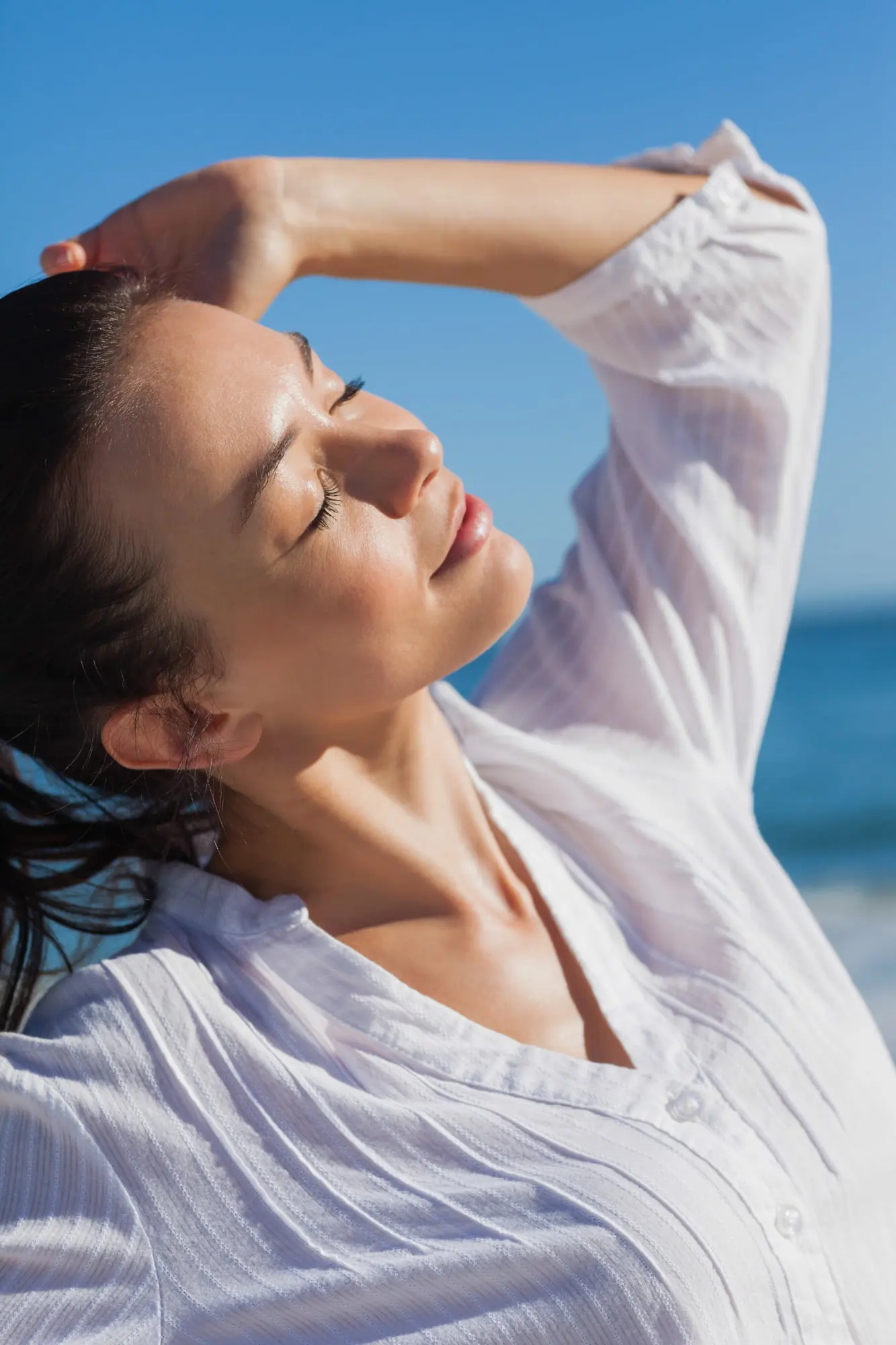 Enjoying the sunlight by the sea, a woman with uneven skin tone stands with eyes closed near Refresh MedSpa in Cape Coral, FL.