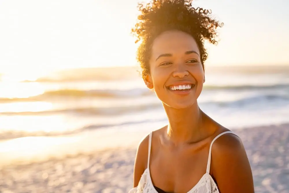 Woman smiling on a sunny beach with ocean waves in the background, radiating confidence after her Botox Cape Coral FL treatment.