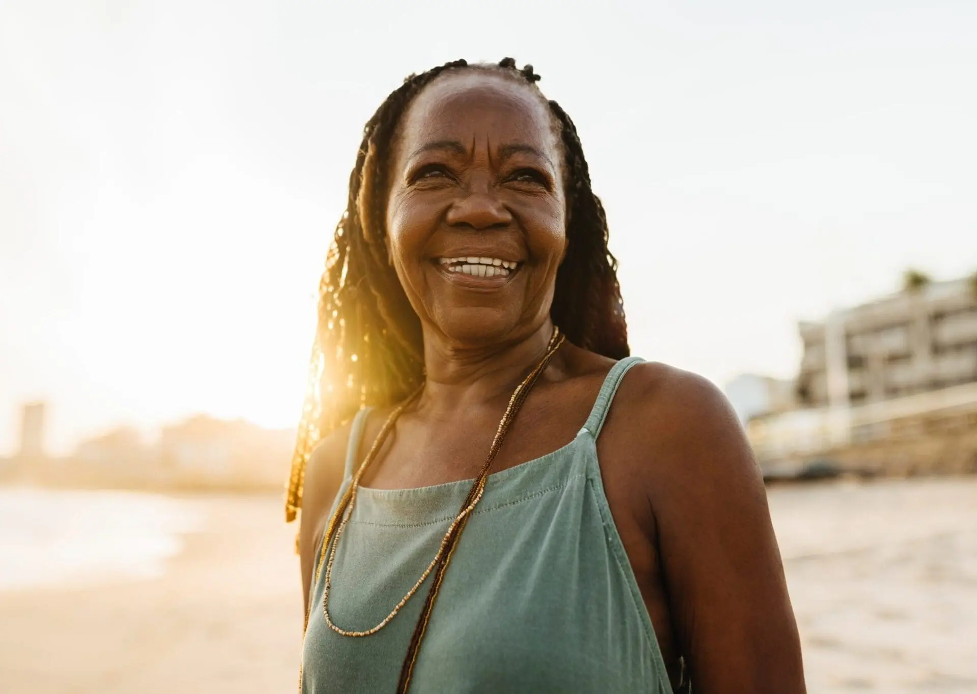 Smiling mature woman with locs in mint green top, showcasing natural volume and lift from Radiesse treatment at Refresh MedSpa