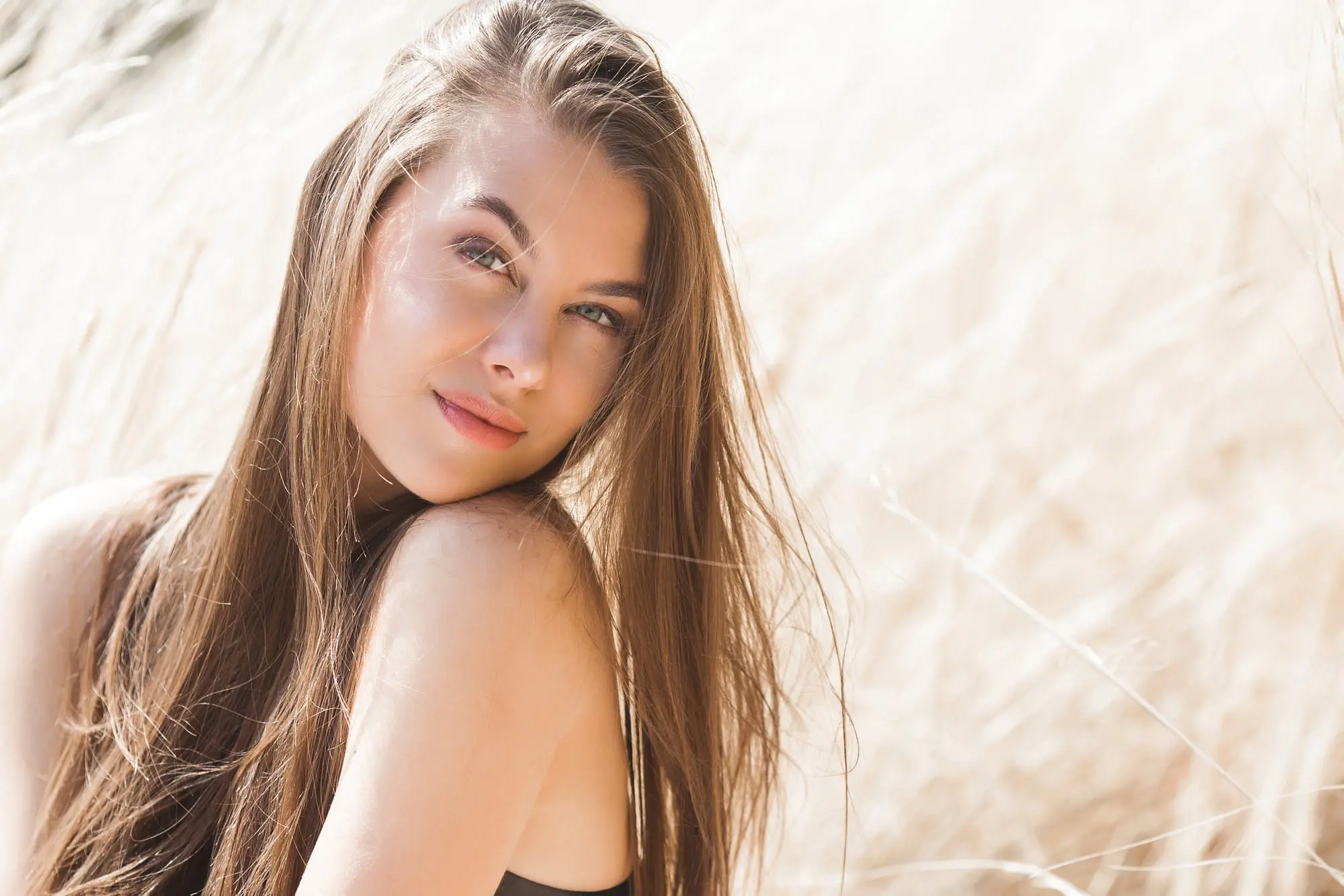 A woman with long brown hair poses confidently before tall grass, reflecting Refresh MedSpa’s spirit.