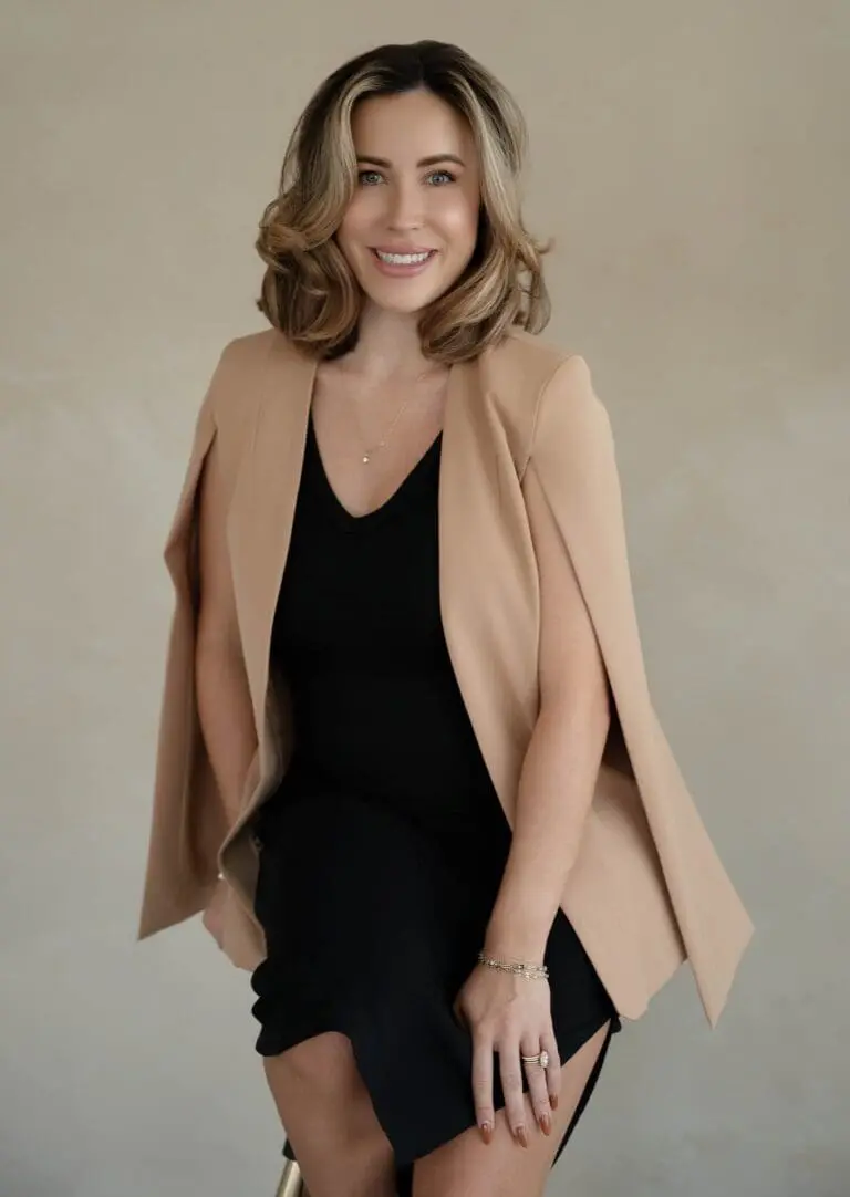 Vanessa Levine NP-C sits on a stool, wearing a tan blazer over a black dress, smiling warmly. She is a Medical Spa expert at Refresh Medspa in Cape Coral, FL.