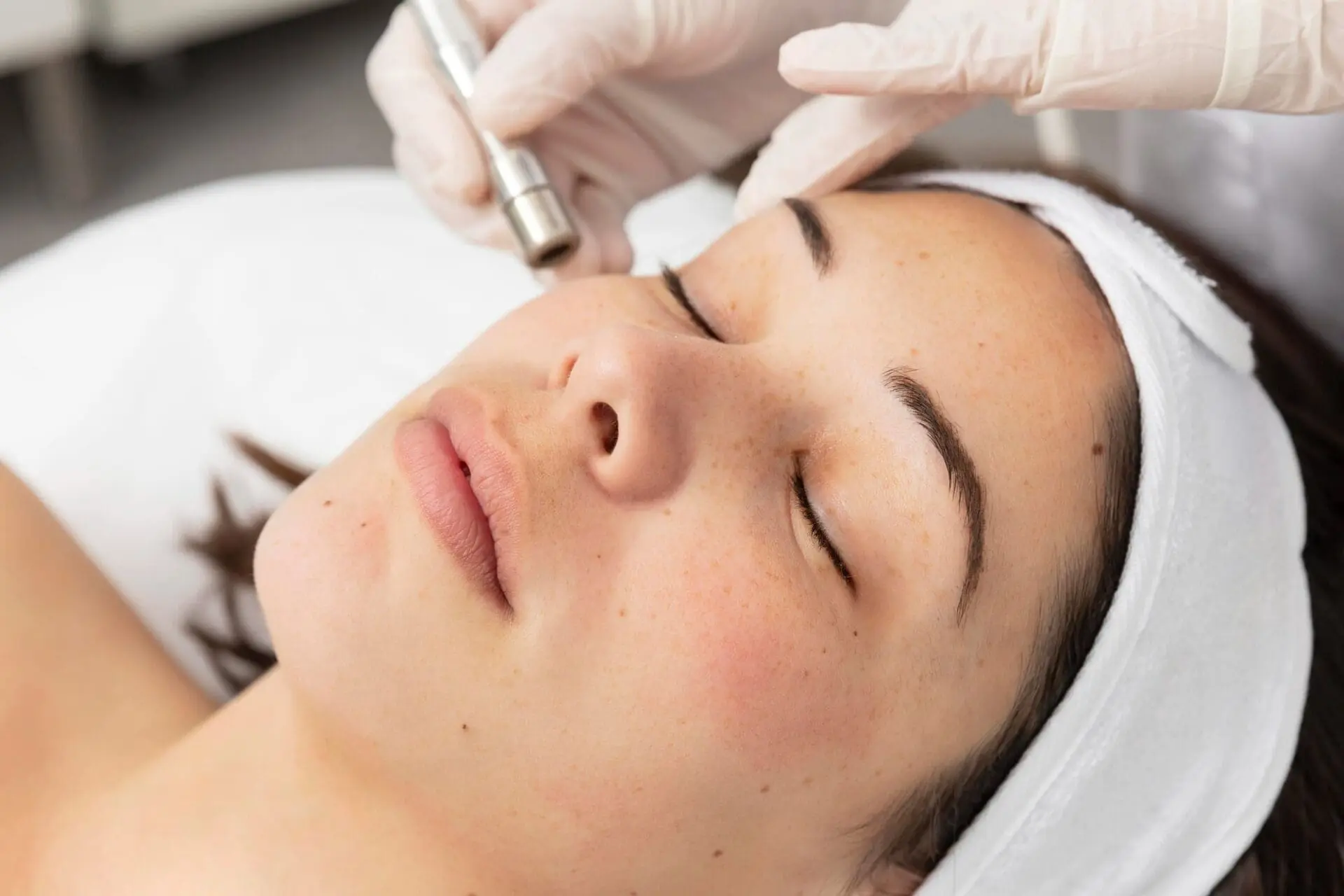 At Refresh MedSpa in Cape Coral, FL, a person wearing a white headband receives a facial treatment as a gloved hand uses a handheld device near their cheek.