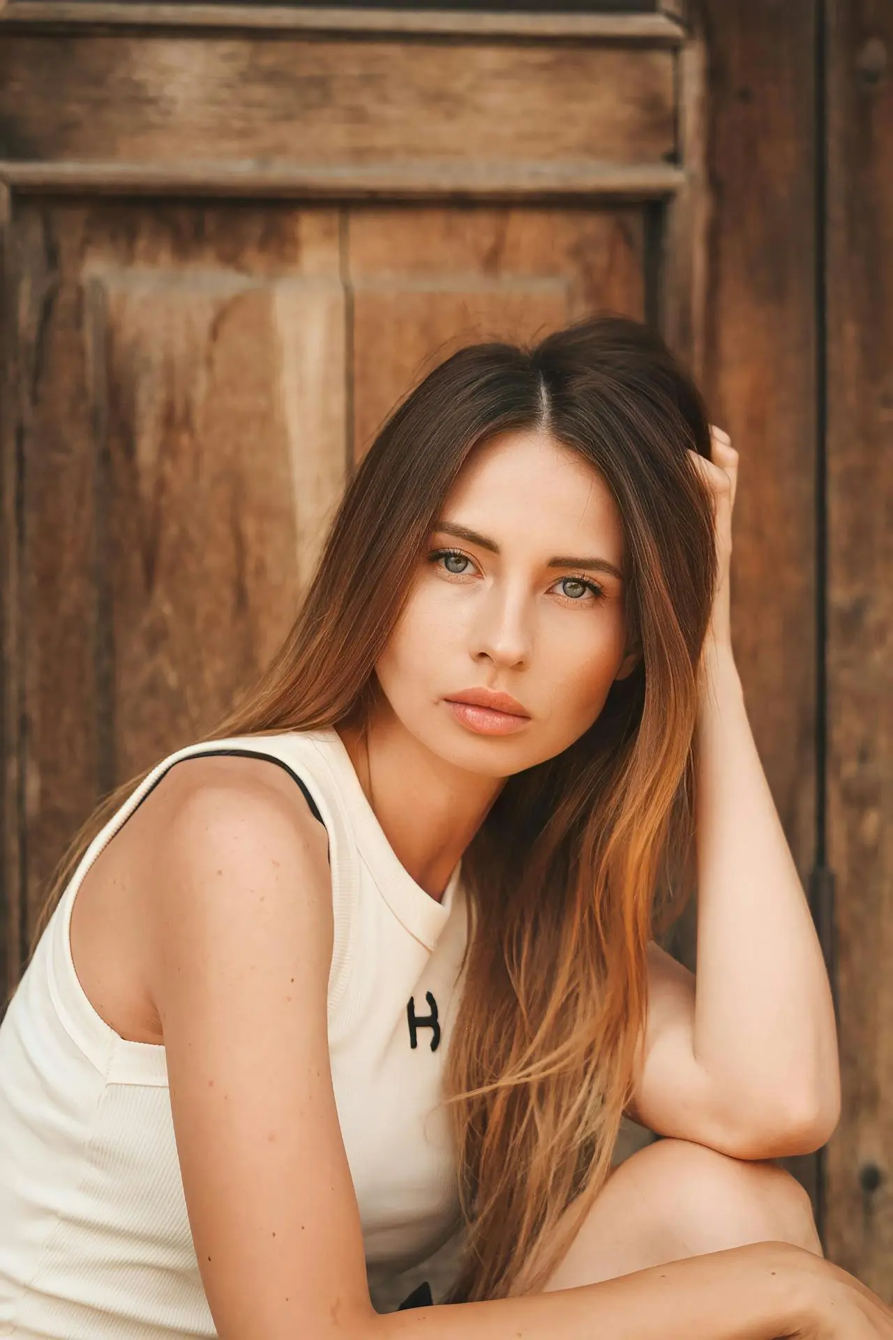 At Refresh MedSpa, a woman with long brown hair and a white top sits by a wooden door with a natural look.