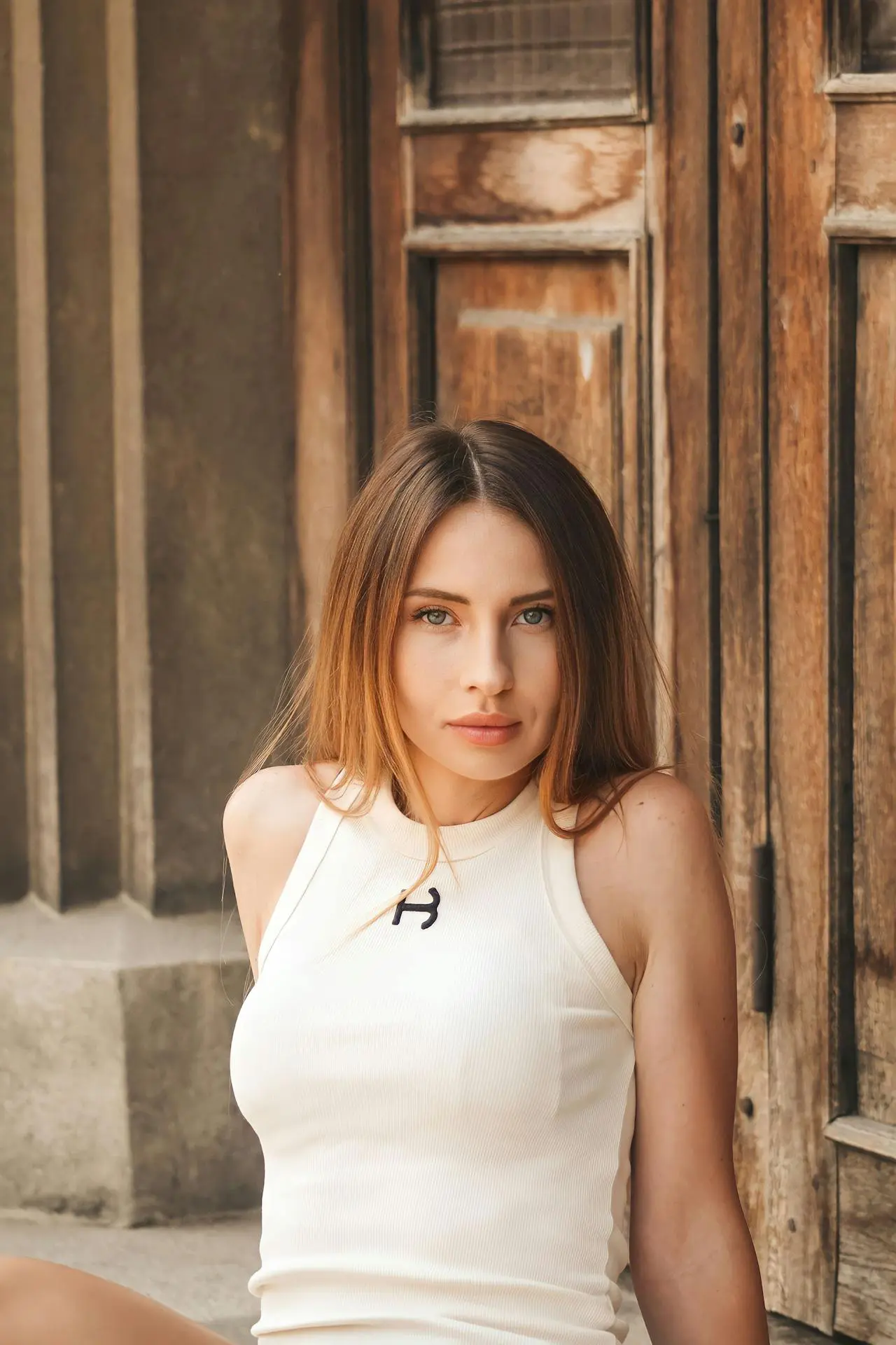 A woman with long brown hair and a white sleeveless top sits by a wooden door, radiating the glow from Refresh MedSpa.