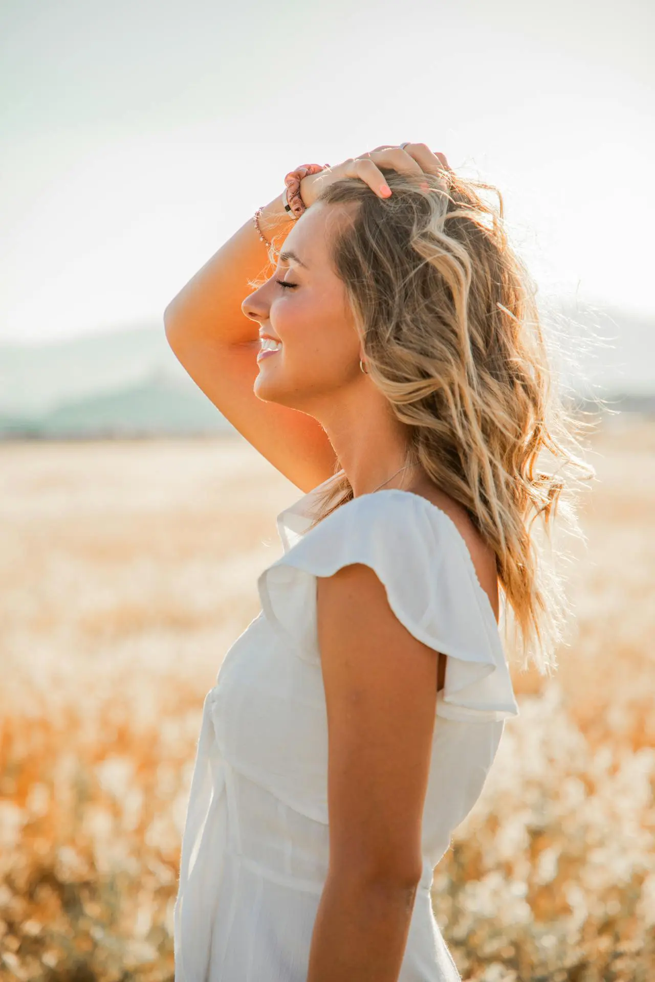 A confident woman in white smiles in a sunlit field, showcasing Dysport results at Refresh MedSpa.