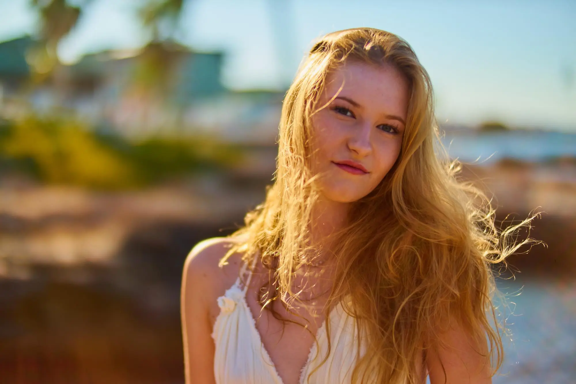 A young woman with long blonde hair glows after Juvederm at Refresh MedSpa, outdoors by greenery and water.