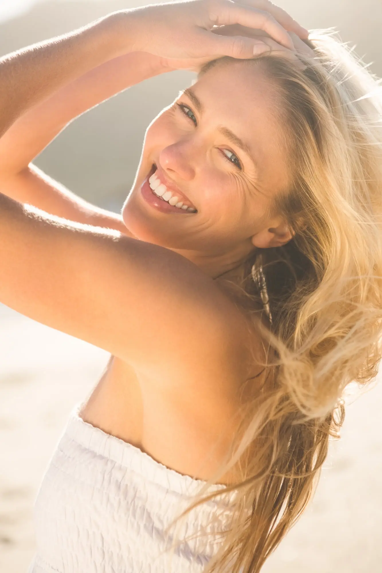 Smiling woman with long blonde hair outdoors, confident after Radiesse at Refresh MedSpa, in white strapless top.