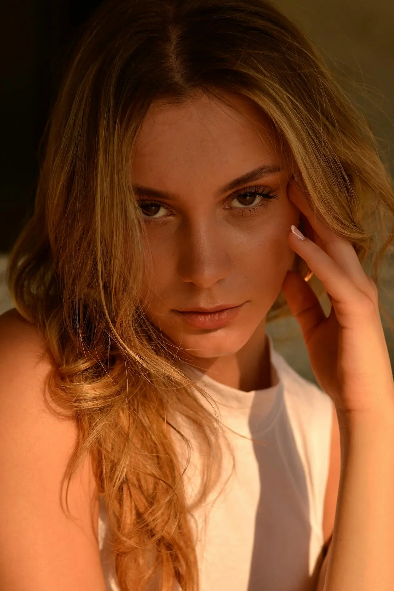 A woman with glowing skin, long light brown hair, and a white sleeveless top poses at Refresh MedSpa.