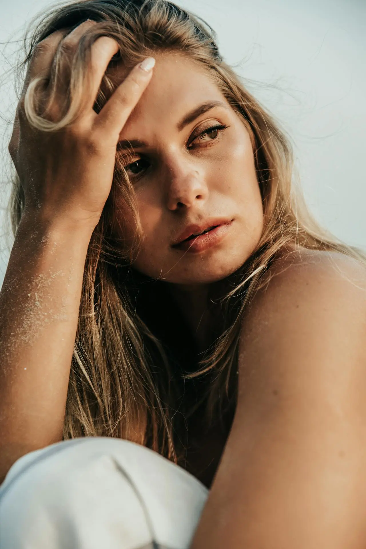 A woman with long blonde hair and sandy skin looks thoughtfully to the side, her glow reflecting Refresh MedSpa.