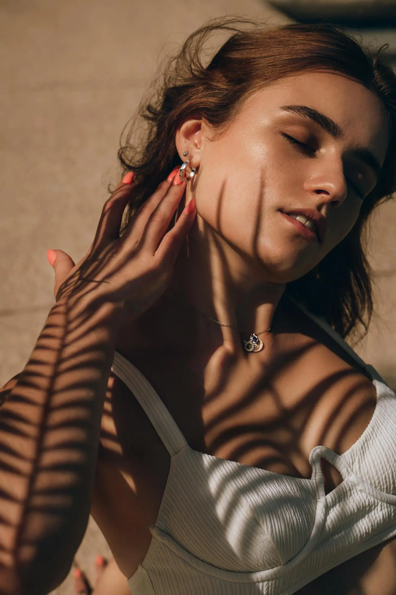 At Refresh MedSpa, a woman in a white top closes her eyes and touches her neck as palm leaf shadows grace her skin.