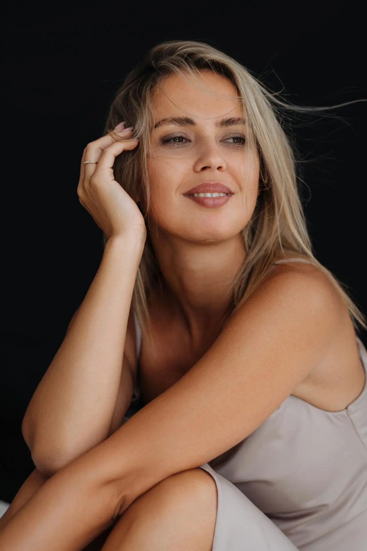 A woman with blonde hair sits in a light sleeveless top, showing natural beauty after Restylane at Refresh MedSpa.