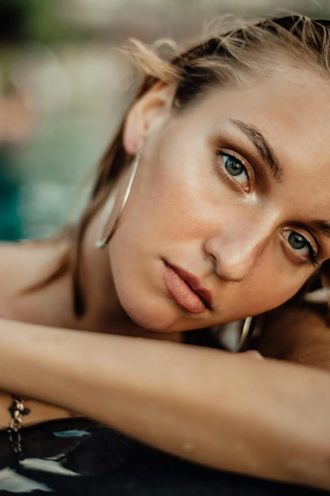 A young woman with hoop earrings and wet hair at a pool showcases smooth, refreshed skin after wrinkle relaxers at Refresh MedSpa.