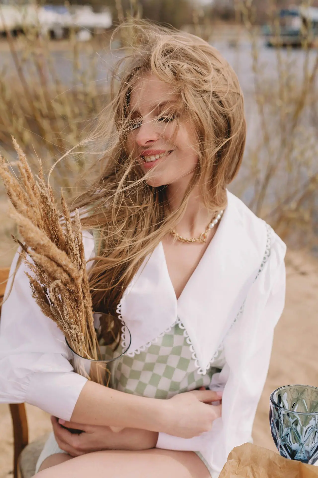 Outdoors at Refresh MedSpa, a woman with long hair and wind-swept face holds dried grass, embodying Xeomin elegance.