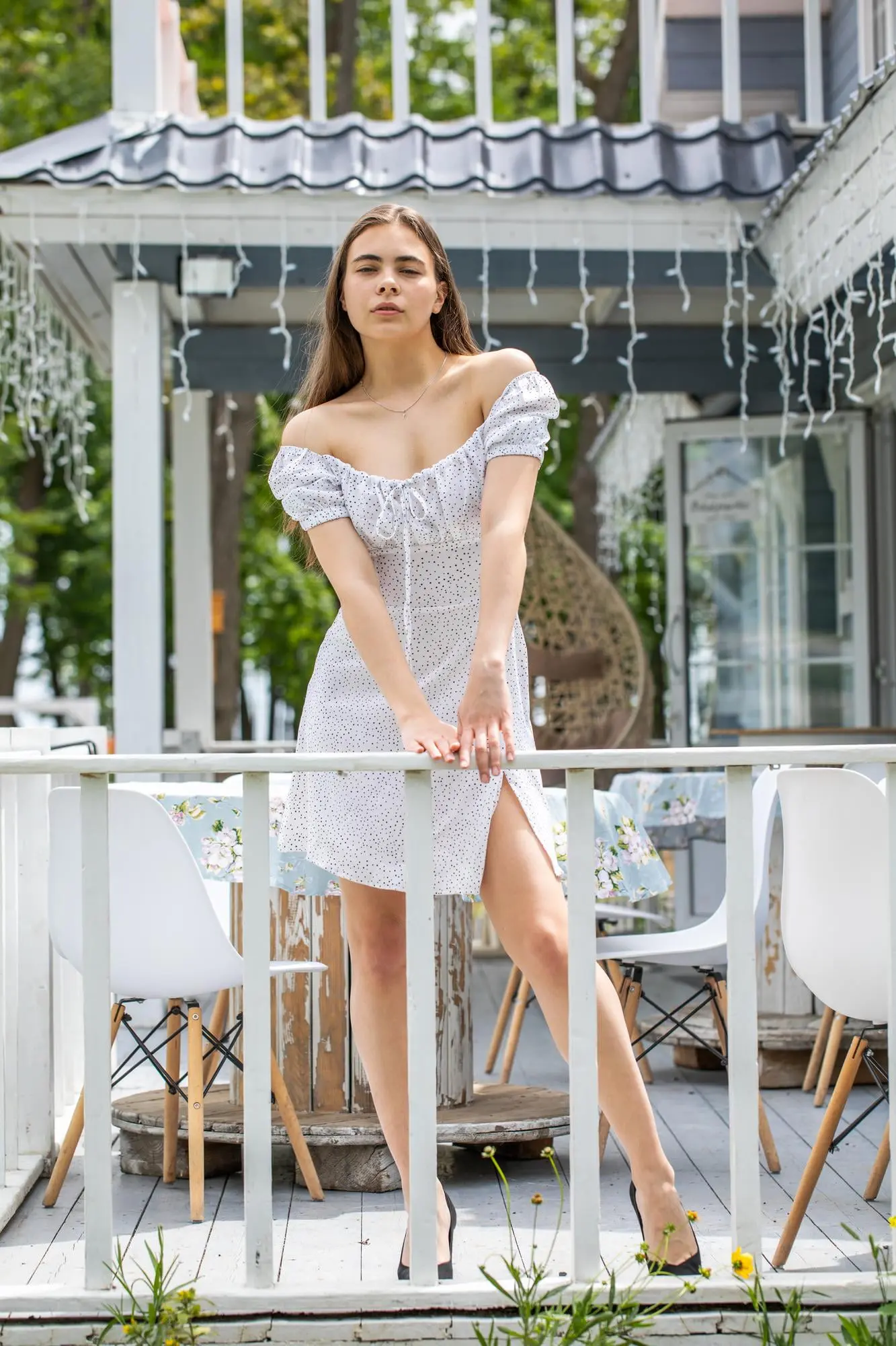 A woman in a white off-shoulder dress glows after a Refresh MedSpa Hydrafacial, on a porch in Cape Coral, FL. Outdoor chairs behind serving clients from Fort Myers.