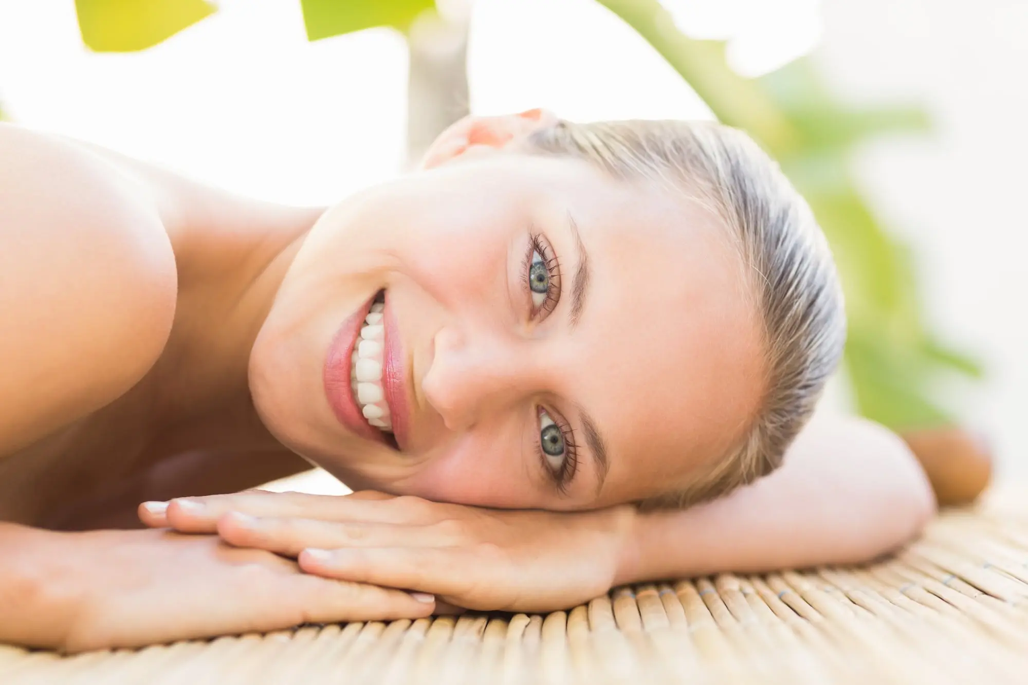 Smiling person with light skin and blue eyes on a woven mat, glowing post-chemical peel at Refresh MedSpa.