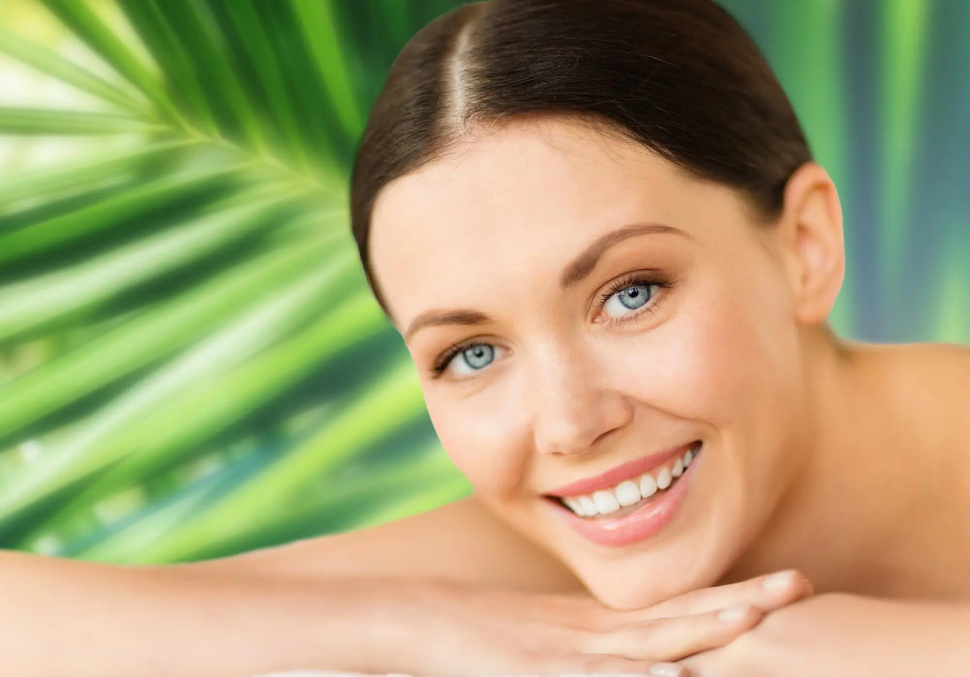 Smiling woman with blue eyes and brown hair, confident after a chemical peel at Refresh MedSpa; green leaf behind.