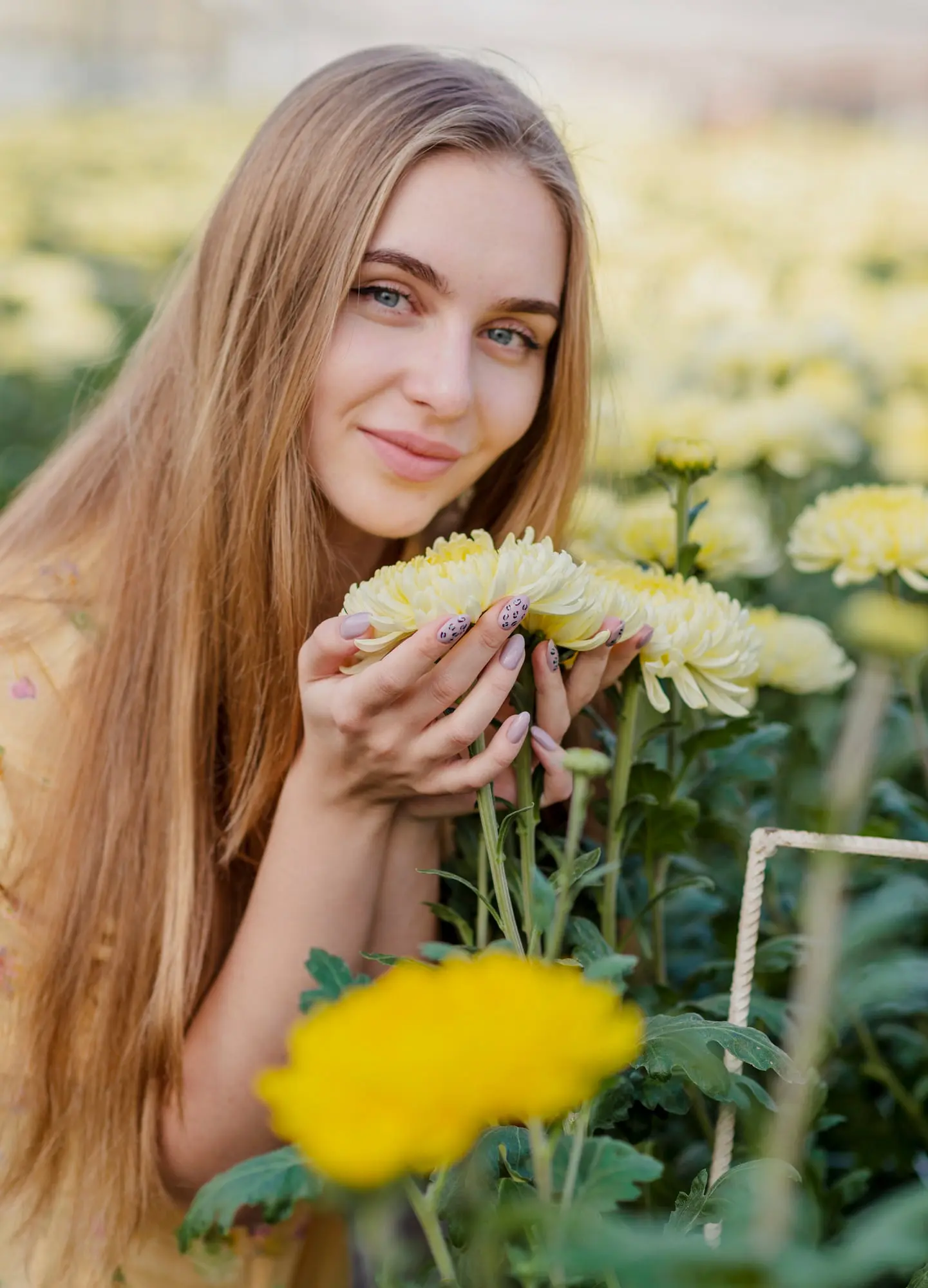 Enjoying pale yellow flowers in a chrysanthemum garden, a woman with long blonde hair glows after her HydraFacial at Refresh MedSpa.