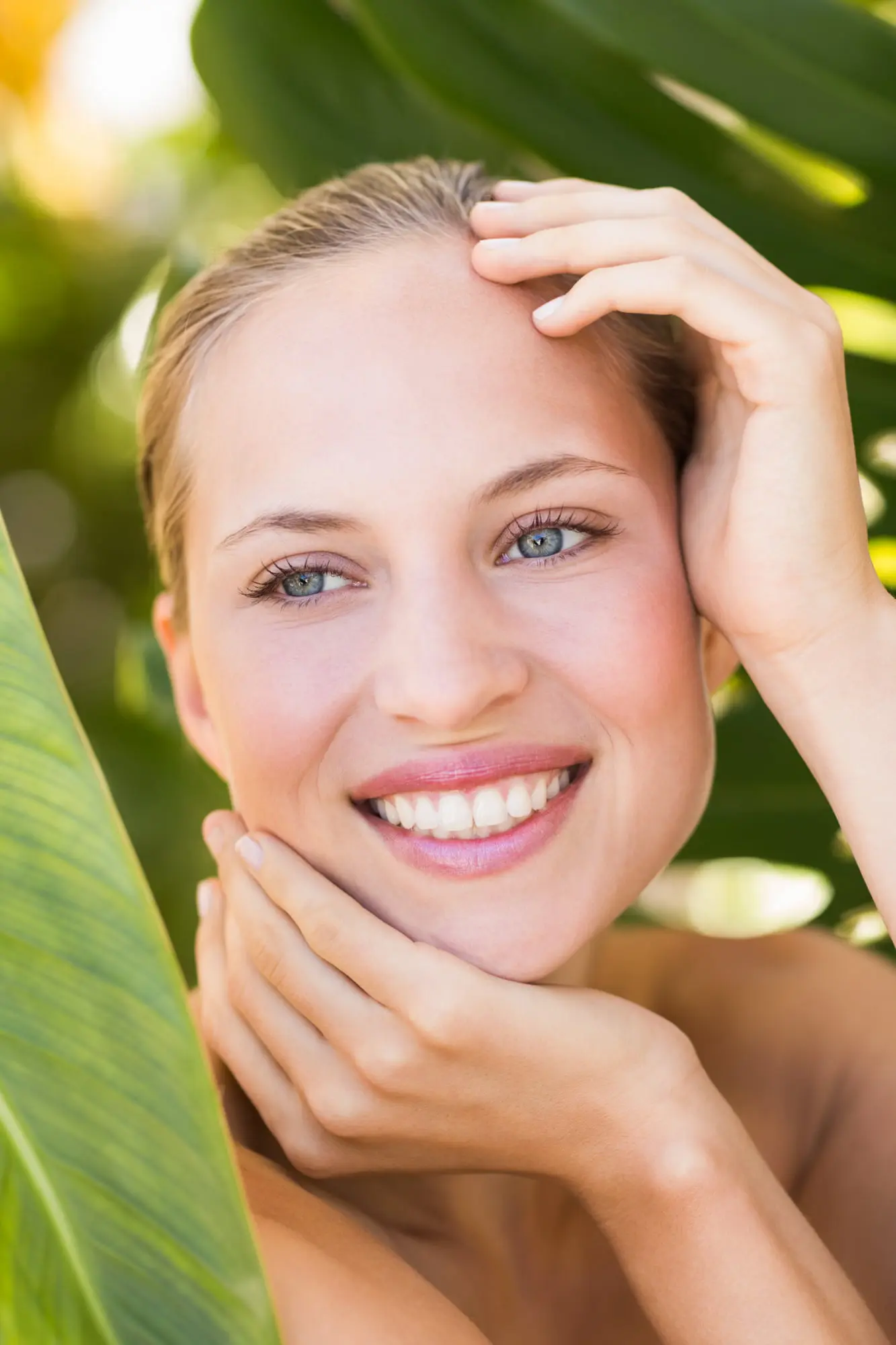 Smiling woman with light skin and blue eyes in green leaves, showing refreshed glow after microneedling at Refresh MedSpa.