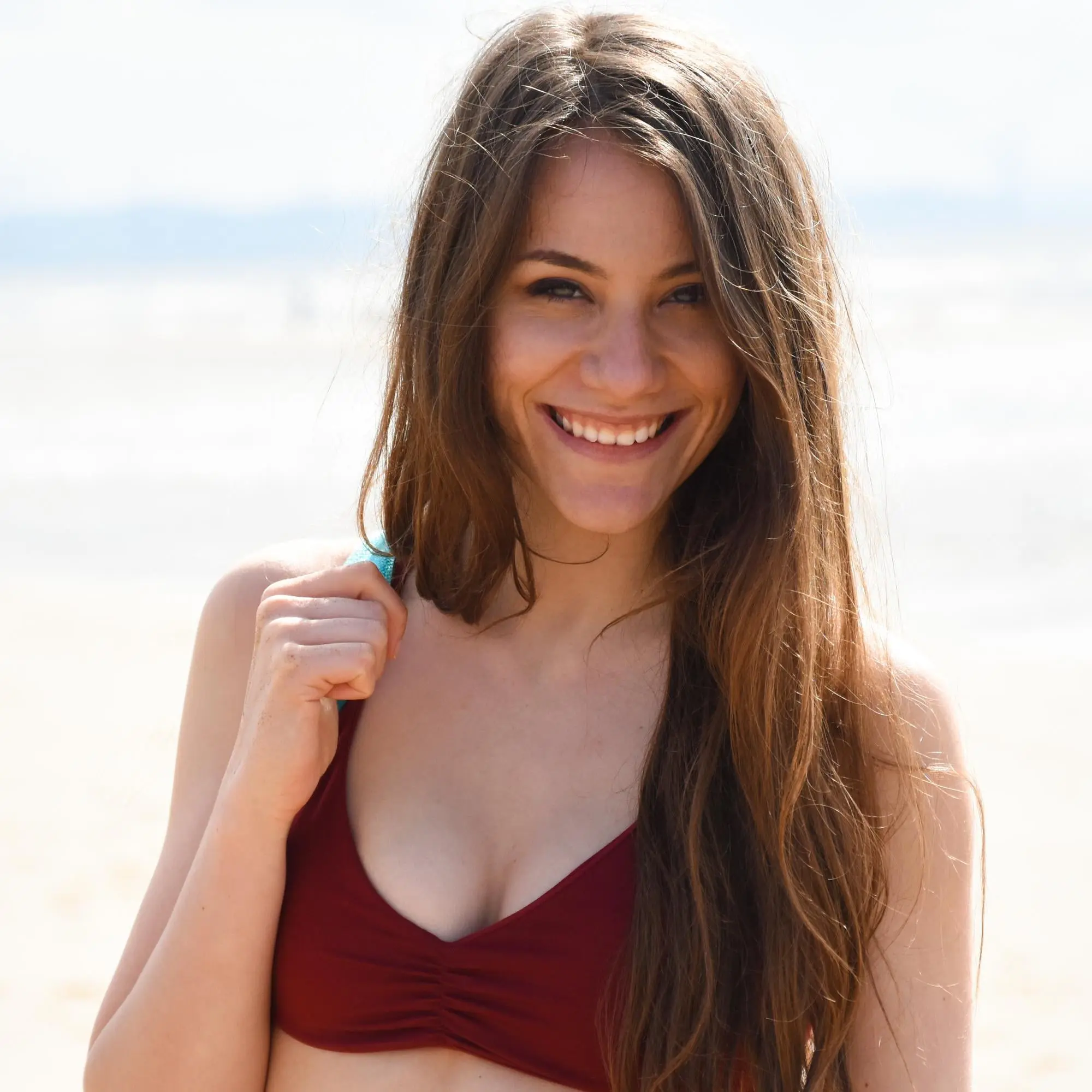 A confident woman with long brown hair in a burgundy bikini top smiles for Refresh MedSpa.