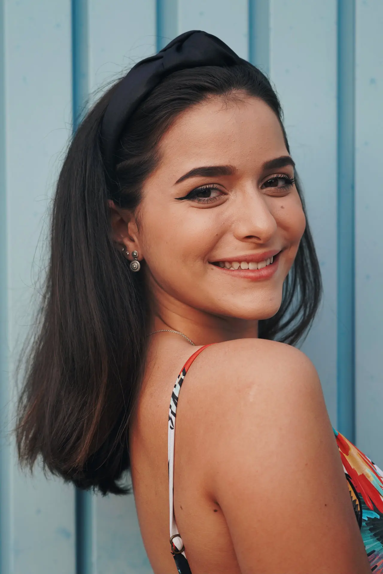 Smiling woman with dark hair, headband, and patterned top on light blue background—Botox confidence at Refresh MedSpa in Cape Coral, FL.