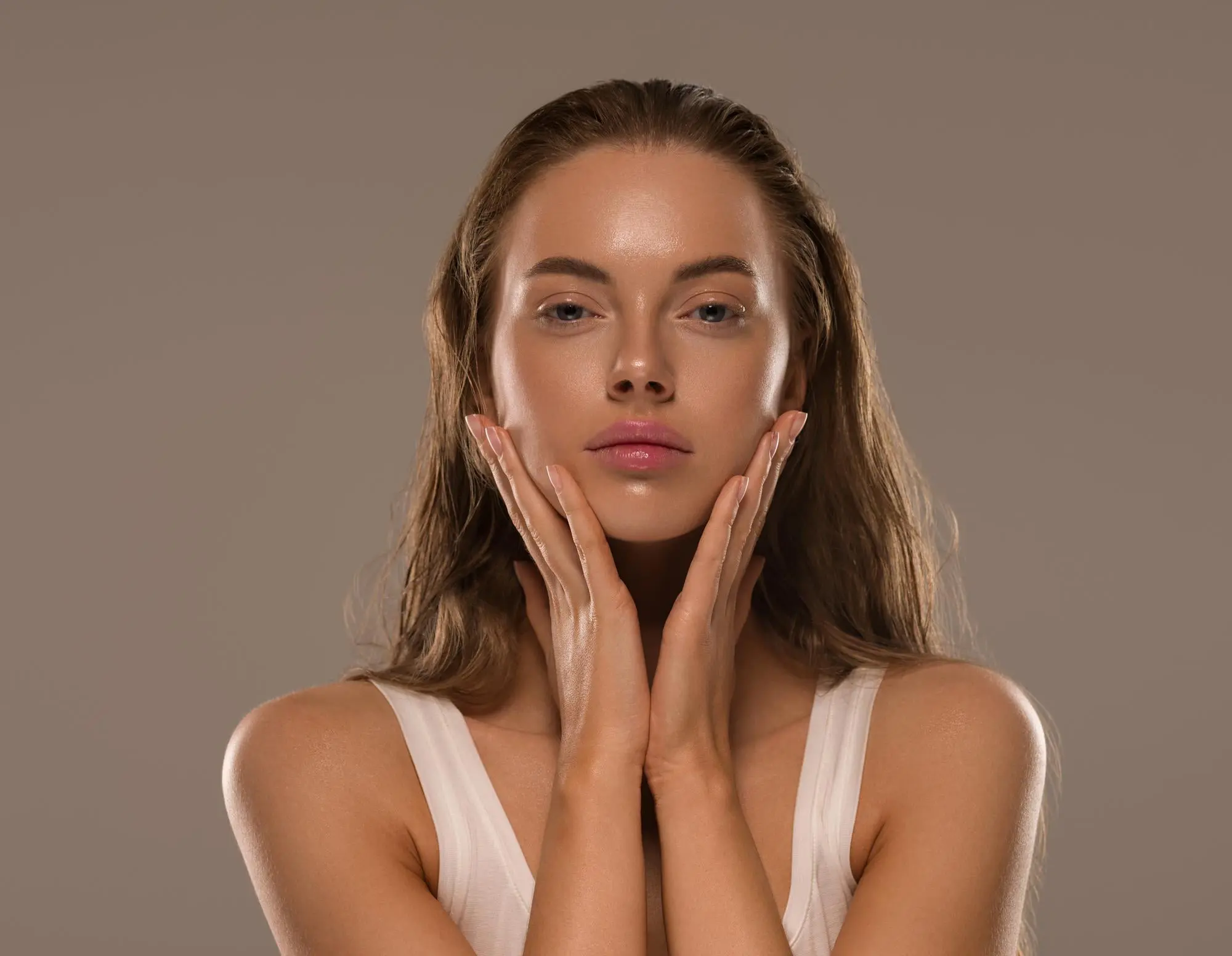 A person with long brown hair touches their face, looking at the camera, and may seek acne scars treatment at Refresh MedSpa in Cape Coral, FL.