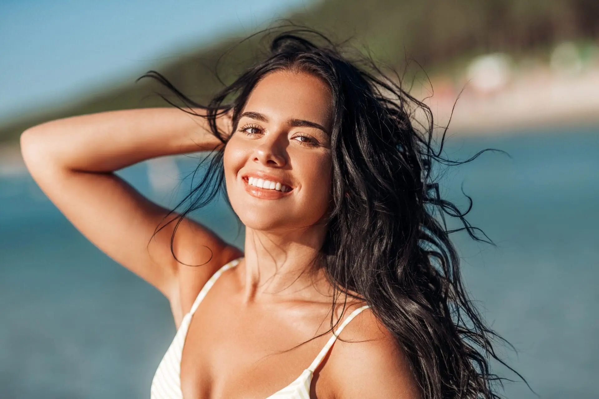 Smiling woman with long dark hair by the water in Cape Coral, FL, shows off glowing HydraFacial skin from Refresh MedSpa.