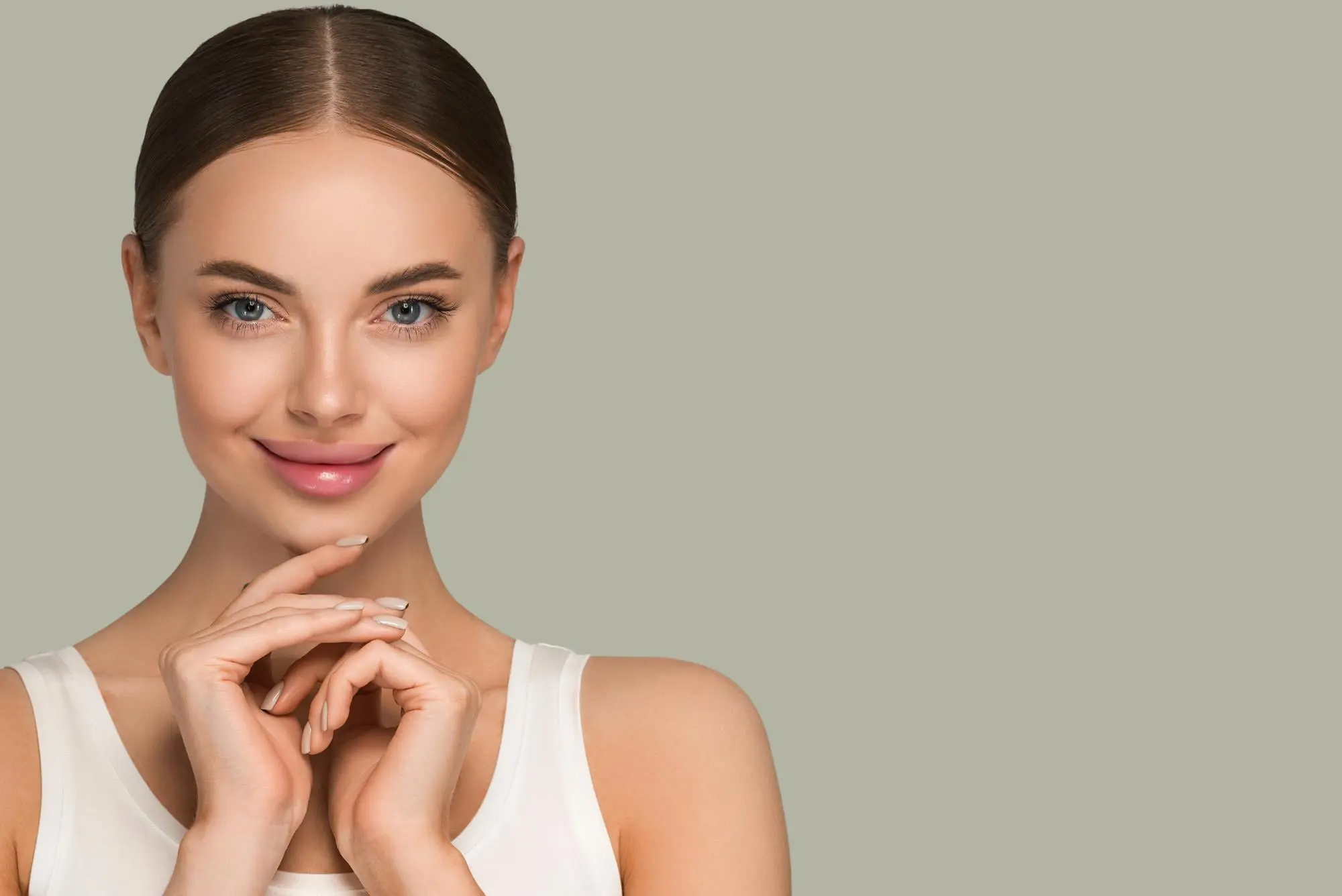 Smiling young woman with brown hair in a sleek bun, white tank top, at Refresh MedSpa in Cape Coral, FL against a light gray background.
