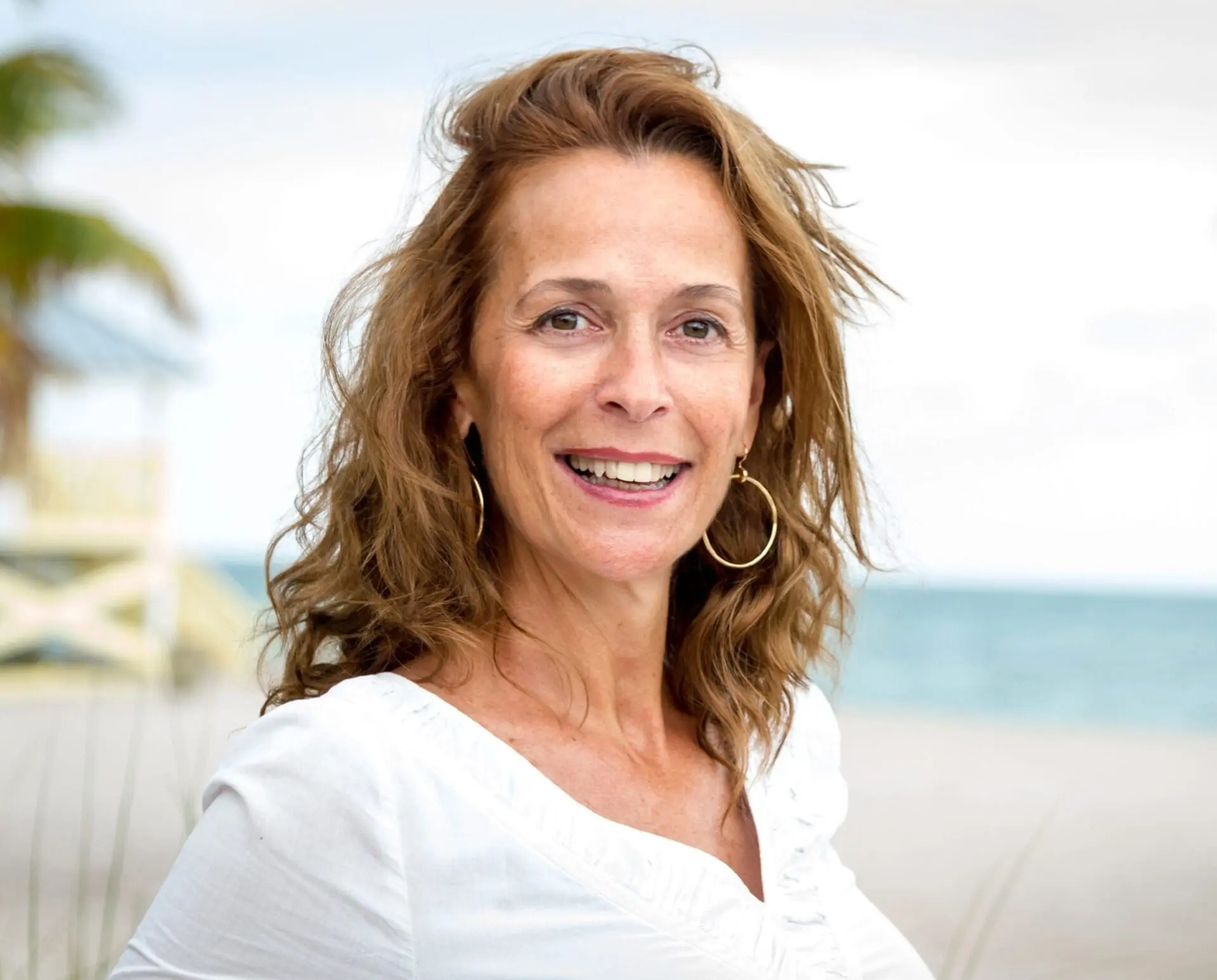 Smiling woman with wavy brown hair on a Cape Coral beach, radiant after Radiesse at Refresh MedSpa in Cape Coral, FL.