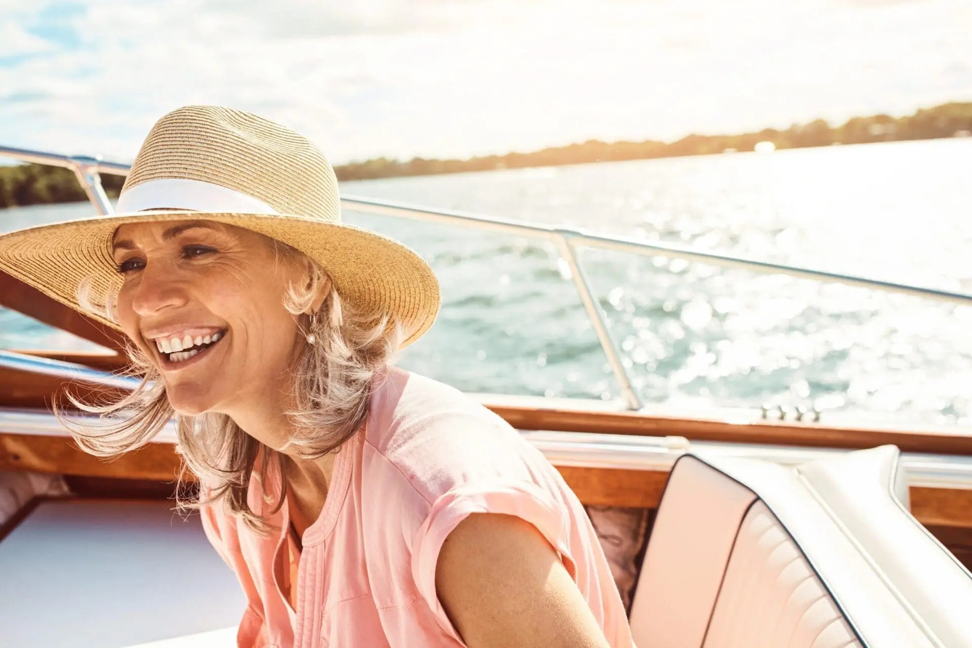 A confident, smiling woman in a straw hat on a sunlit boat promotes youthful glow with Refresh MedSpa in Cape Coral, FL.