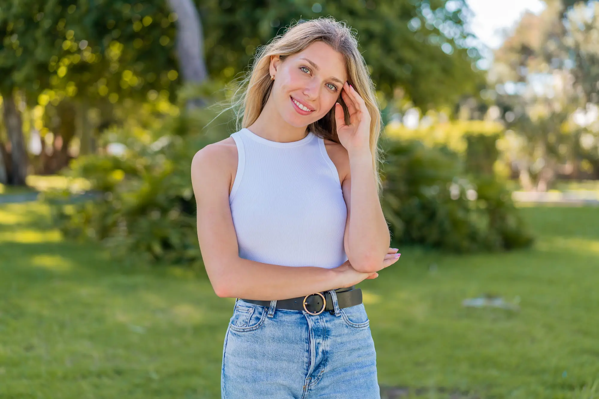 Smiling after her visit to Refresh MedSpa in Lehigh Acres, FL, a blonde woman stands in a sunny green park wearing casual attire.