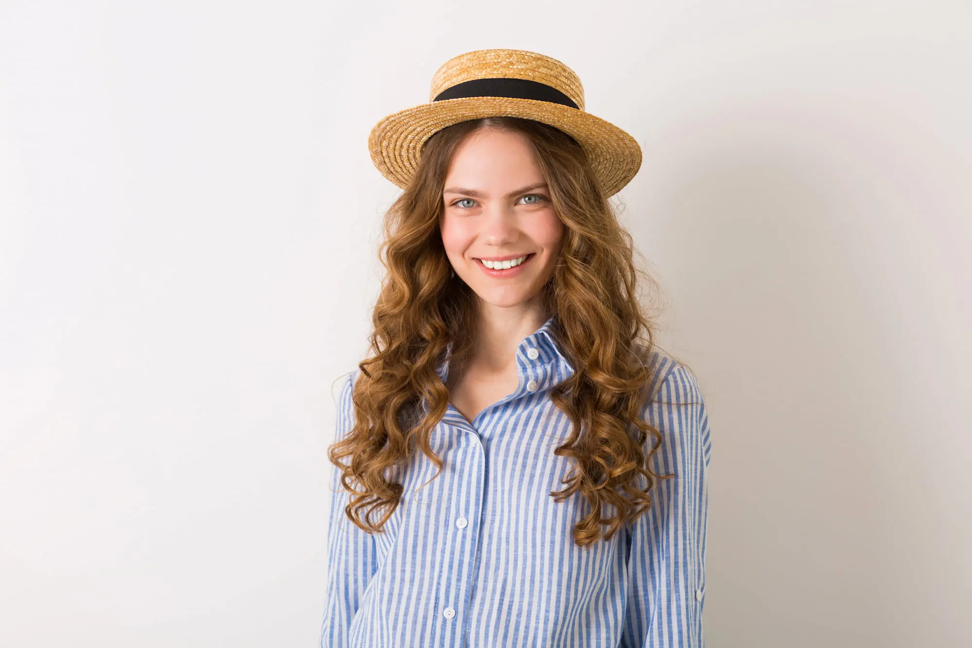 A person with long curly hair in a striped shirt and straw hat smiles confidently, reflecting a Refresh MedSpa visit in Lehigh Acres, FL.