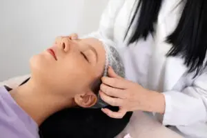 At Refresh MedSpa in Cape Coral, FL, a person with eyes closed has a white hair cover adjusted before a Xeomin vs Dysport treatment.