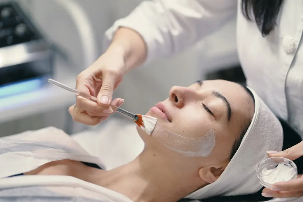 At Refresh MedSpa in Cape Coral, FL, a person relaxes with eyes closed while a practitioner applies white cream to their face using a brush, illustrating a typical chemical peel treatment.