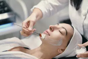 At Refresh MedSpa in Cape Coral, FL, a person relaxes with eyes closed while a practitioner applies white cream to their face using a brush, illustrating a typical chemical peel treatment.
