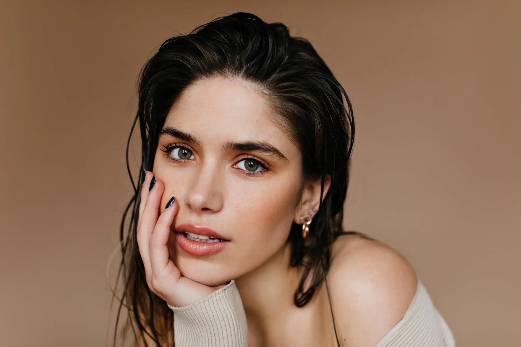 A woman with wet hair rests her face on her hand, gazing at the camera against a beige background, as if considering skincare options at Refresh MedSpa in Cape Coral, FL such as Hydrafacial vs Chemical Peel.