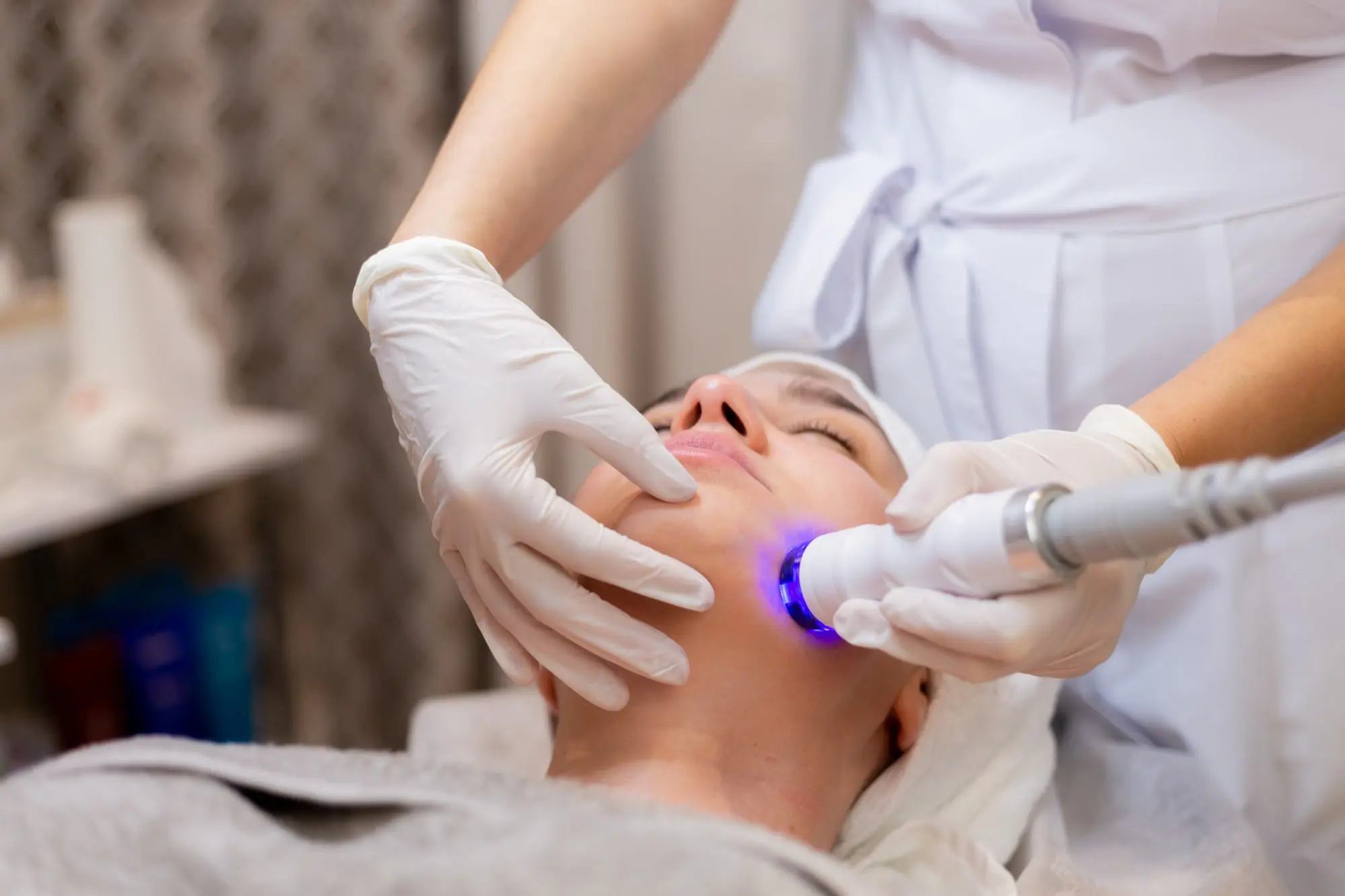 At Refresh MedSpa in Cape Coral, FL, a person receives a facial treatment with a handheld device emitting blue light, contemplating how many BBL sessions are needed to see results.