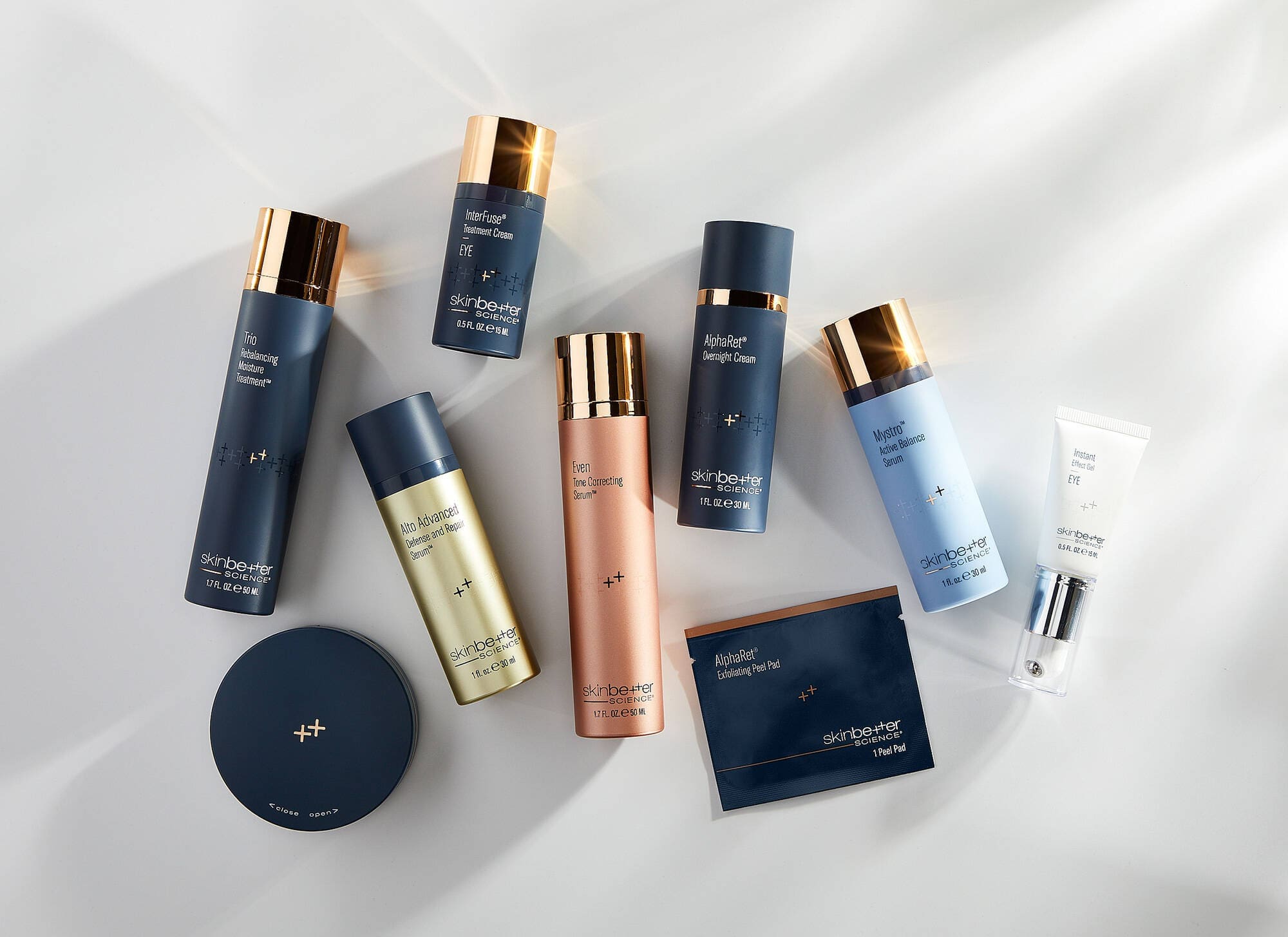 A flat lay of various skincare products in bottles and tubes with gold caps, elegantly displayed on a light gray surface, reminiscent of the sun-kissed beauty found in Cape Coral, FL.