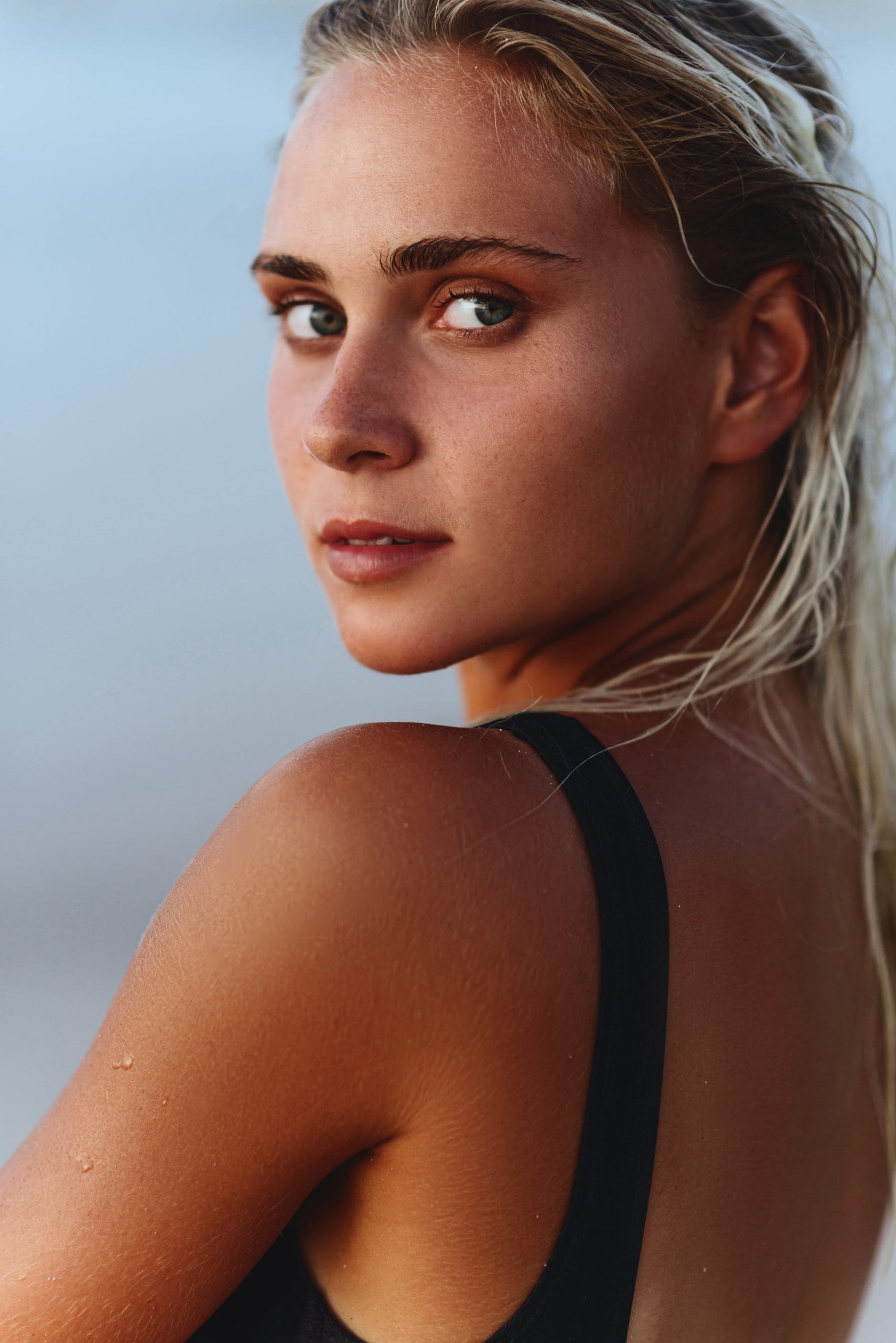 At Refresh MedSpa in Cape Coral FL, a tanned woman with wet blonde hair in a black swimsuit looks over her shoulder, lips highlighted.